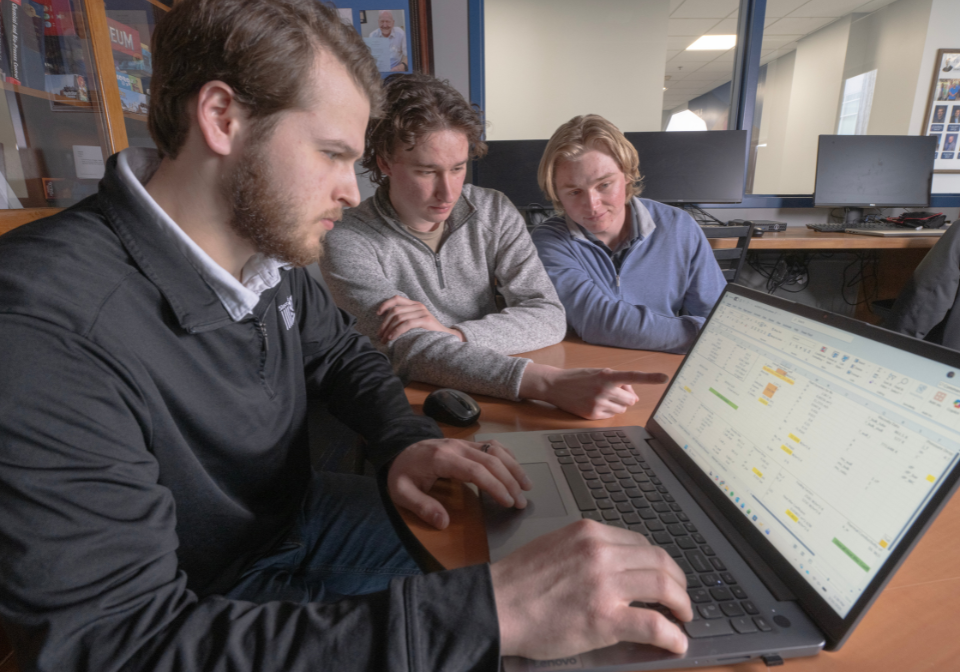 three student gather around a laptop