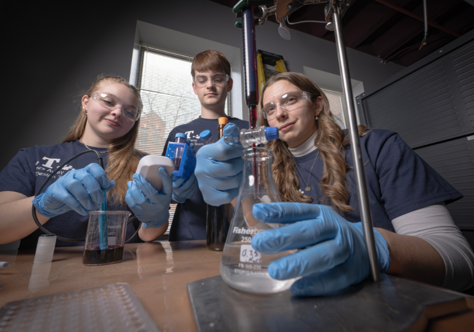three students check various liquids in beakers