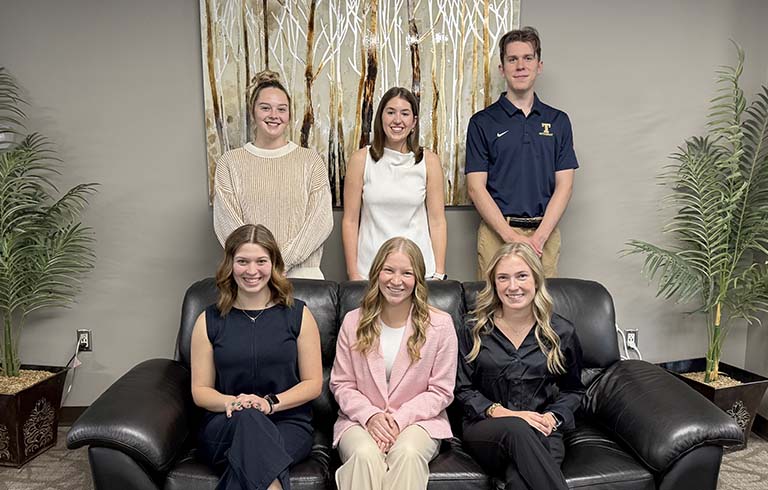 Three students seated on couch with three students standing behind them