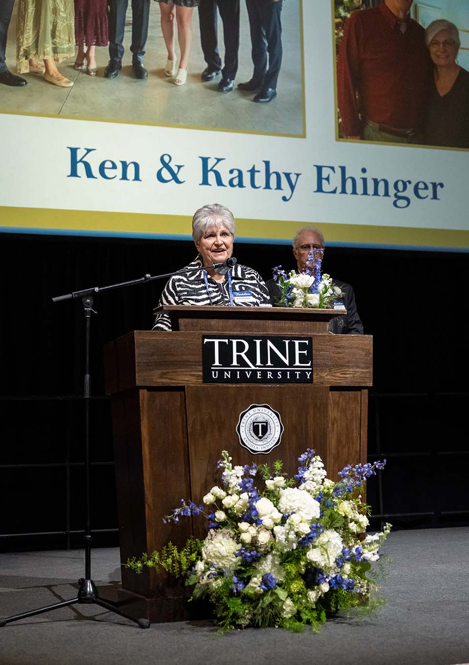 Kathy Ehinger speaking at podium with Ken Ehinger standing behind