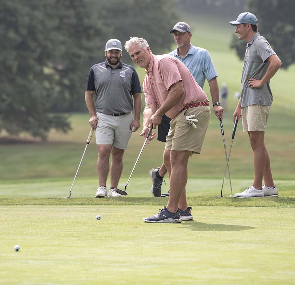 Man putting on a golf course as three others watch