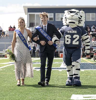 Woman and man in crowns and sashes walking arm-in-arm with white tiger mascot.