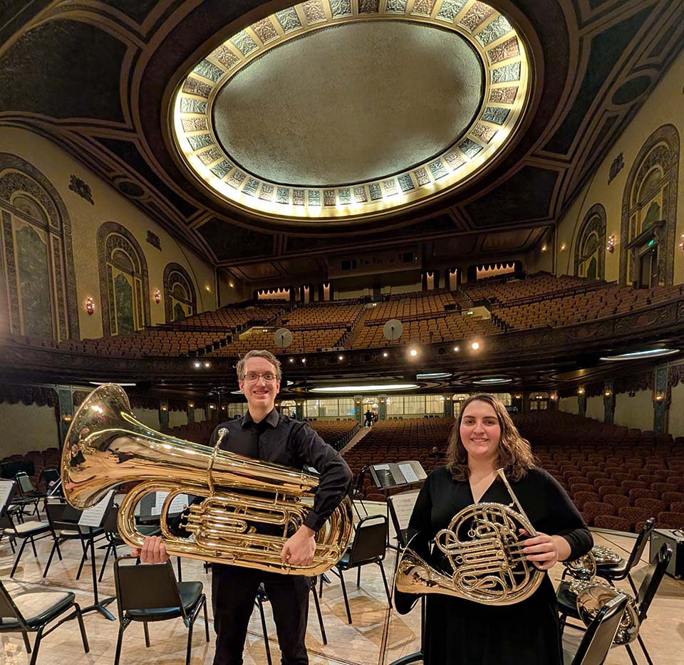 Male student with tuba and female student with French horn on the stage of the Ambassy Theatre