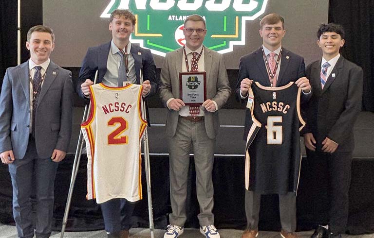 Students and faculty advisor with plaque and jerseys from sports sales competition