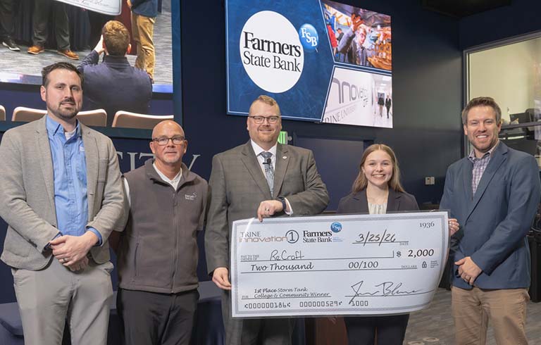 Three bank officials and college administrator presenting large check to student.