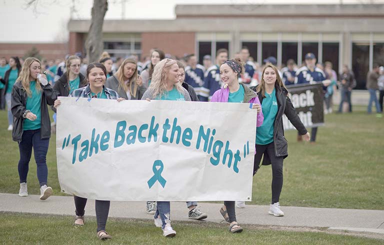 Students walking across campus with a Take Back the Night banner