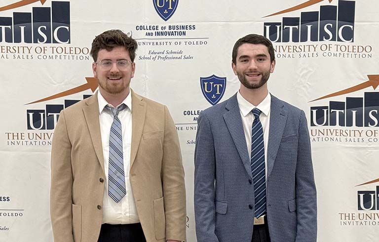 Jacob Seier and Carson Sickmiller standing in front of UTISC banner